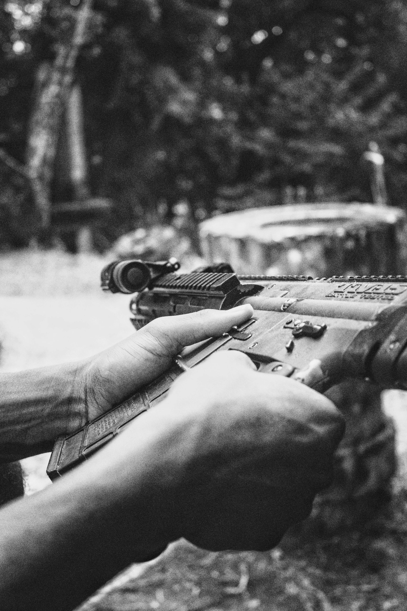 Black and white photo of hands holding a rifle outdoors, emphasizing grip and detail.